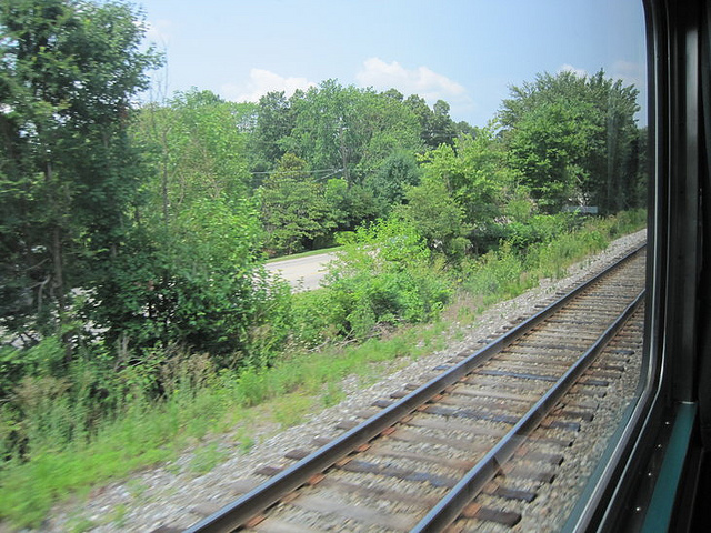 View of train tracks from outside train window grass and trees