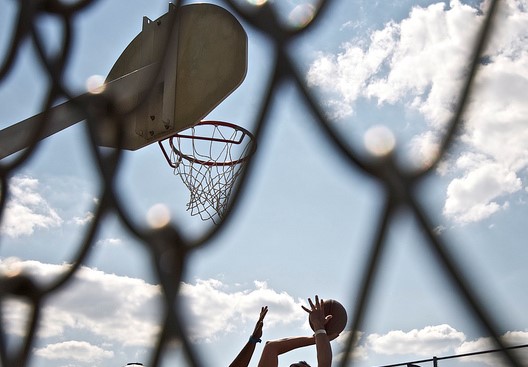 Image of a basketball hoop with someone taking a shot image is through a hole in a chainlink fence