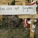 wooden in crosses in field with a note that says you are not forgotten on one