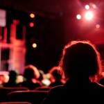 blurry image of heads facing a theatre stage
