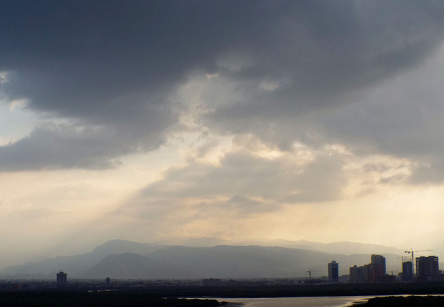 dark rain clouds and rain with a little light peeking through over city in UAE, mountains in distance