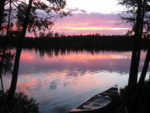 canoe on side of lake, sunset in back