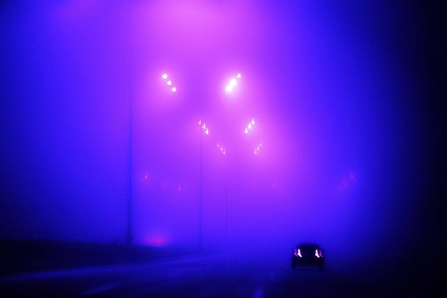 car alone on highway, taillights on, bright street lights in blue and purple