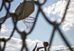 image of a basketball hoop with someone taking a shot, image is through a hole in a chainlink fence