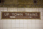 tiles on subway statopm wall and sign that says up town train with arrow pointing to the right