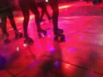 Legs and roller skates on a lit dance floor of a roller disco. Shot with an iPhone.