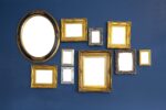 Many size and style of empty picture frames hung on blue wall