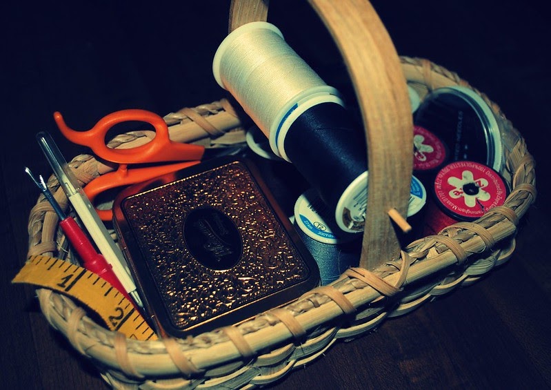 basket of sewing supplies, including spools of thread and orange-handled sewing scissors