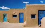three small adobe homes with bright blue doors and big sky