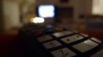 close up of TV remote with blurry TV in the background