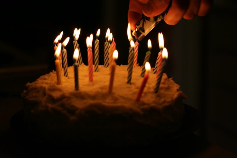 birthday cake with lit candles, hand with lighter, still lighting a few
