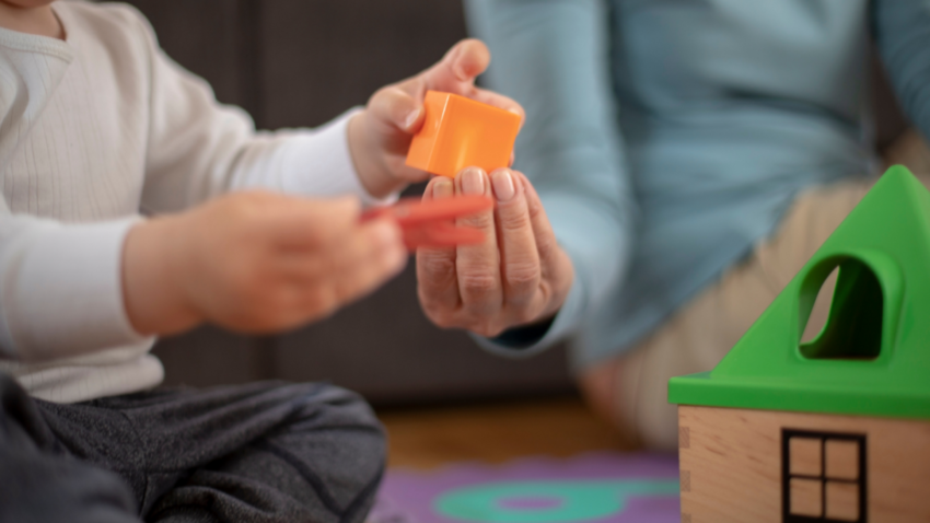 Child and adult hand holding orange block at playset