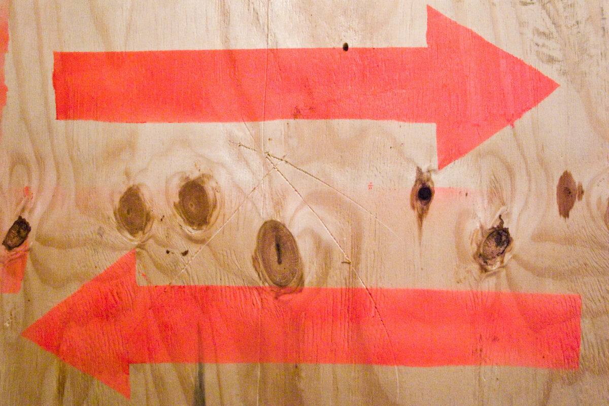 two spray-painted arrows, one right, one left, on sheet of plywood