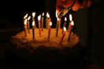 cake with lit birthday candles, a hand reaching out to light