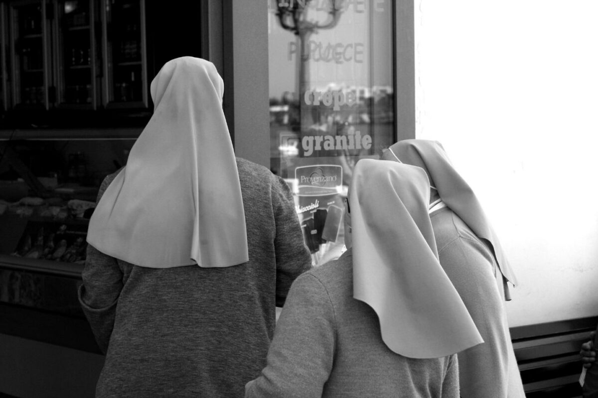 three women in habits (headwear for nuns) from behind, walking into store