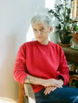 Author Alice Hattrick has short white hair and is wearing a red sweater.