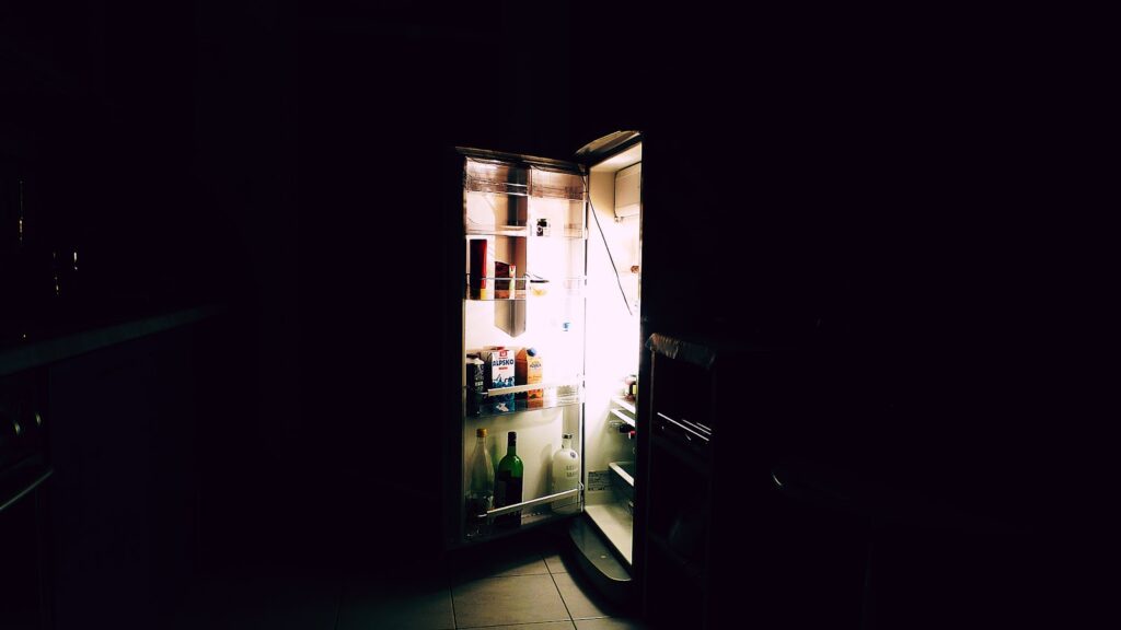 Dark kitchen with fridge door open and light coming out various items inside