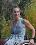 Author Photo of writer Ryan Rae Hardback, a white woman sitting in a wheel chair. She wears a light blue-gray sleeveless shirt.