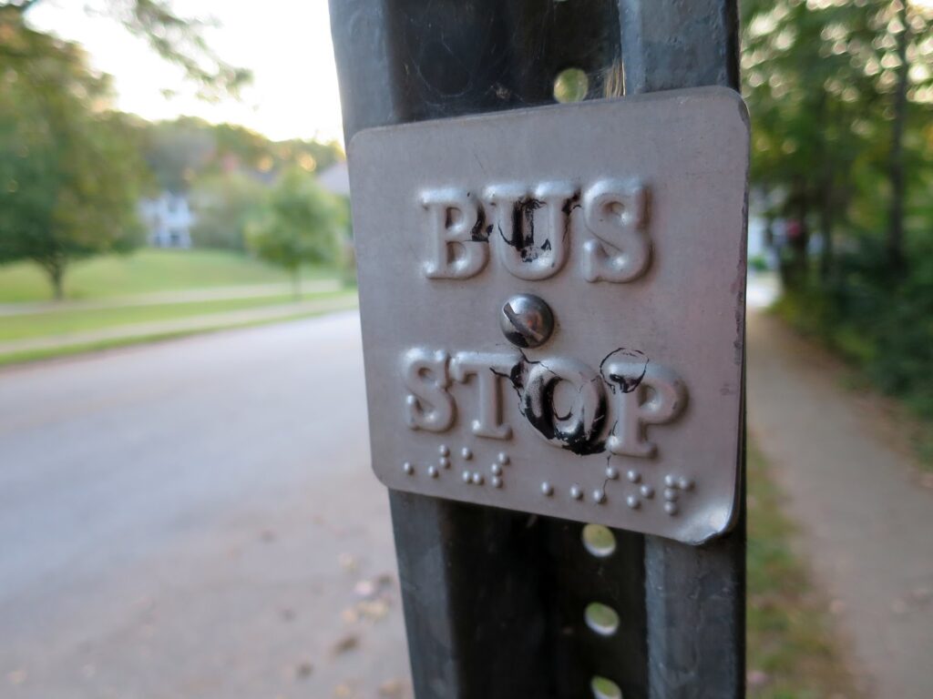 metal plate bus stop sign on sign post, Braille spelling beneath