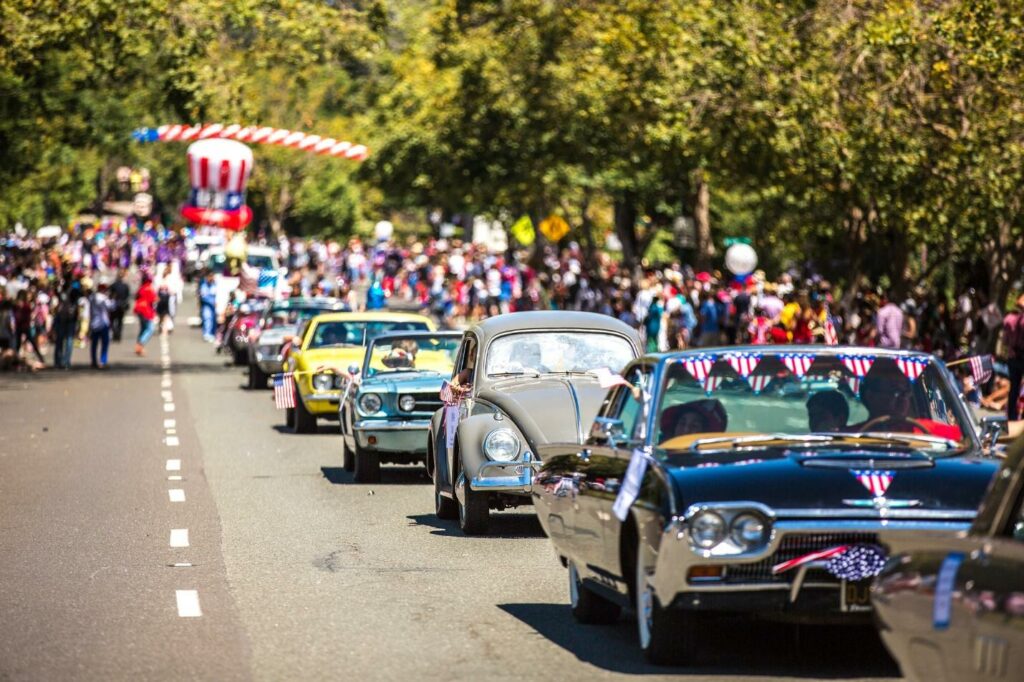 A group of classic cars on a road with a crowd watching parade