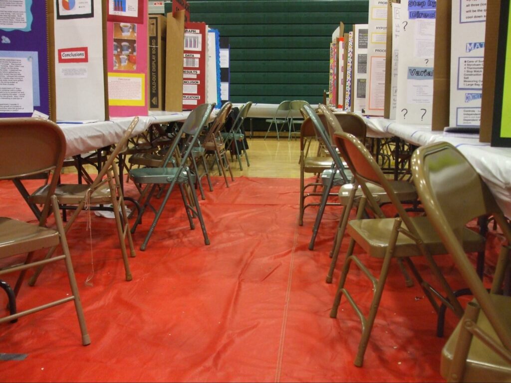 two rows of folding metal chairs and desks with poster presentations (like a science fair) with red carpet between 