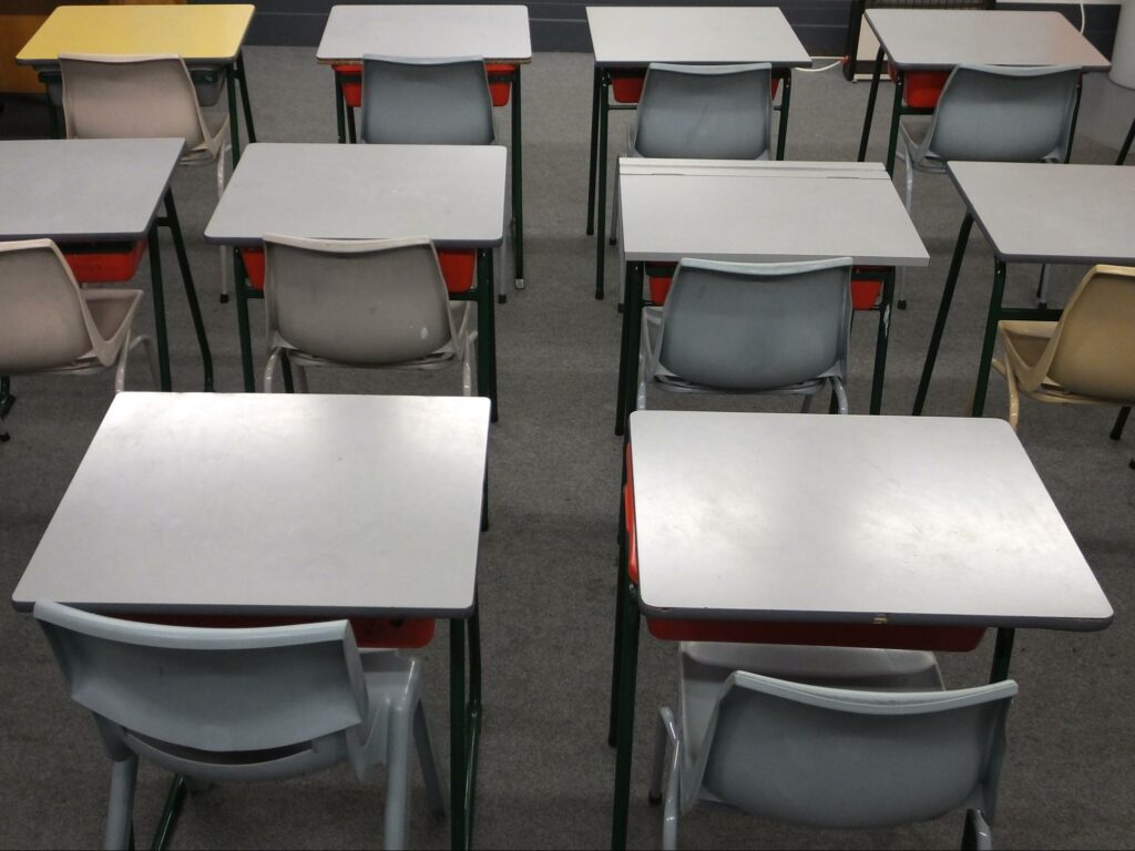 row of empty classroom desks and chairs; sterile vibe