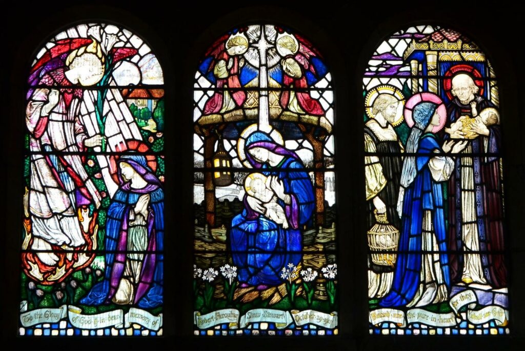 A stained glass windows, three panels each depicting groups of people, including mary and baby jesus