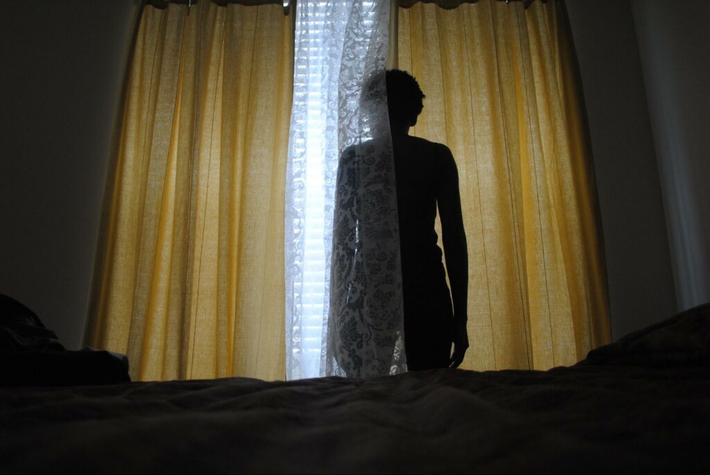 human shadow figure in front of window curtains, looking out