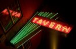 neon sign with the word tavern spelled out with green lines crossing through