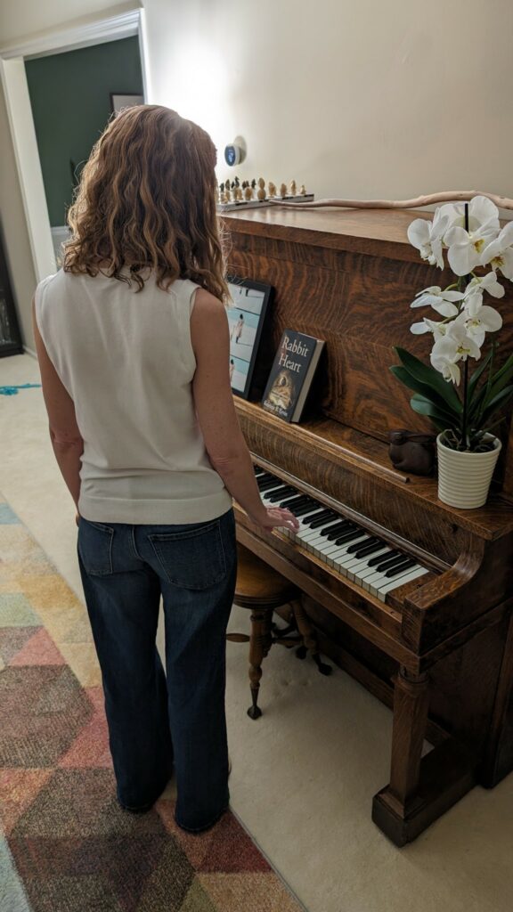 kristine ervin standing at her mother's piano, facing the keys