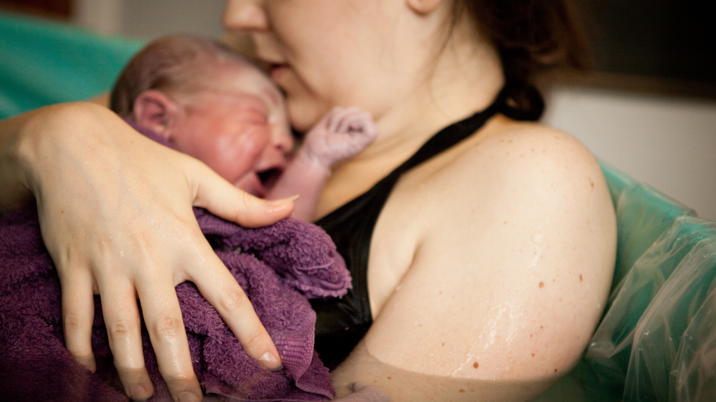 A person holding a newborn crying baby