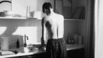 A shirtless man in boxers in kitchen, facing sink
