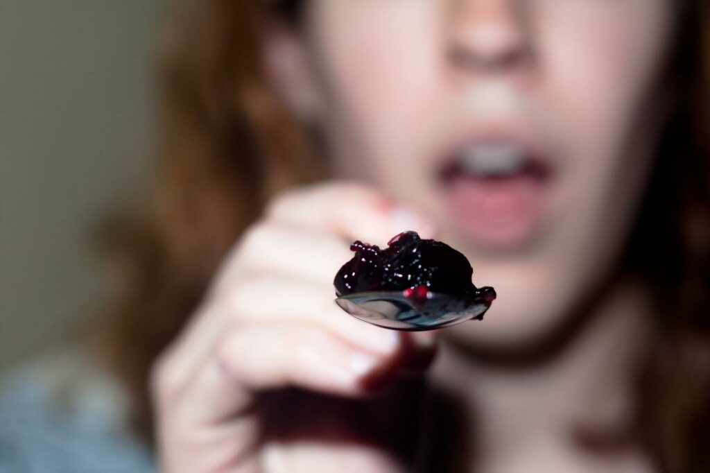 A close-up of a person holding a spoon full of jelly as if feeding someone.