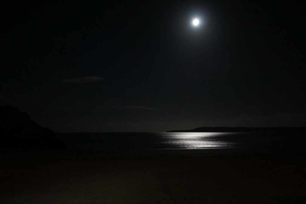 Dark sky with small image of moon in upper right, and reflection below