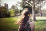 woman facing a tree and field, with her hair blowing in the wind