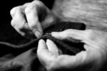 close up image of worn hands making a stitch on a piece of fabric